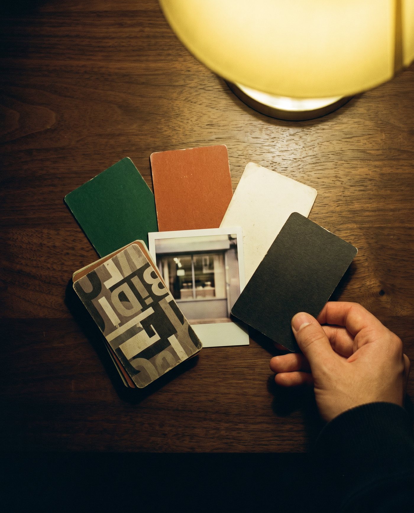 A hand sliding printed identity cards into place on a walnut table under a lamp